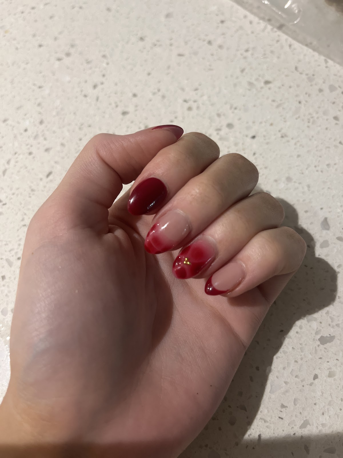 Deep red almond nails with a gold glitter accent